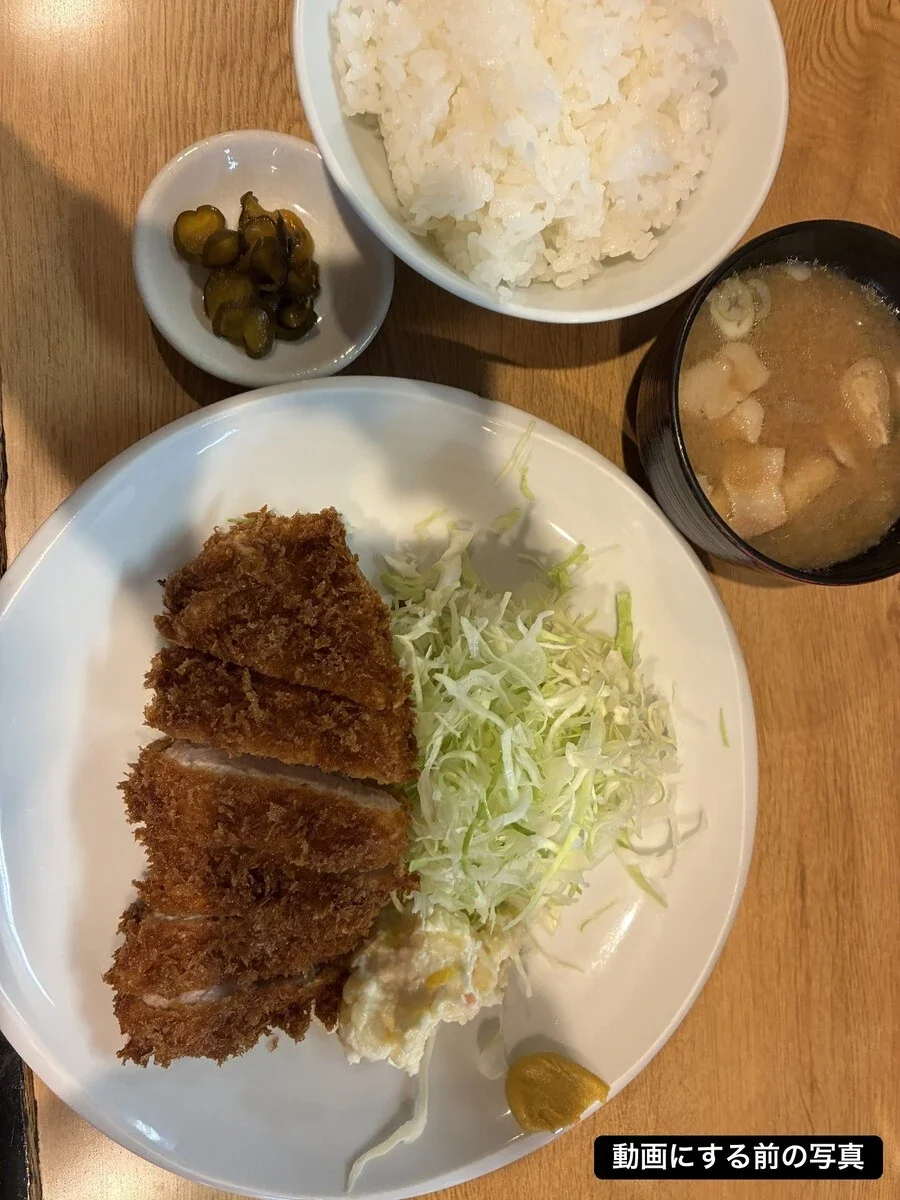 動画にする前のごはん写真。とんかつ定食を真上から撮った1枚で、白い皿にとんかつ、せん切りキャベツ、ポテトサラダ、からしが載り、奥にご飯、漬物、豚汁が並ぶ。右下に「動画にする前の写真」の表示がある
